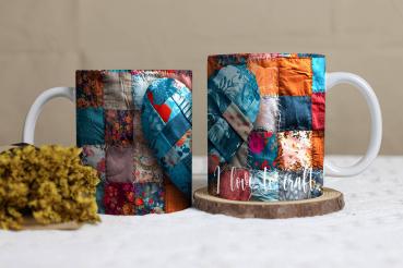 Weißer Keramikbecher mit einem Patchwork-Design in Form eines Herzens. Der Hintergrund besteht aus verschiedenfarbigen Stoffstücken in Blau-, Rot- und Orangetönen. Auf dem Becher steht in einer geschwungenen weißen Schrift: 'I love to craft'. Der Becher l